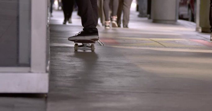 Close view of young man's feet and shoes as he rides a skateboard in Downtown Los Angeles. Other people's feet visible in background. Slow motion recorded at 60fps.