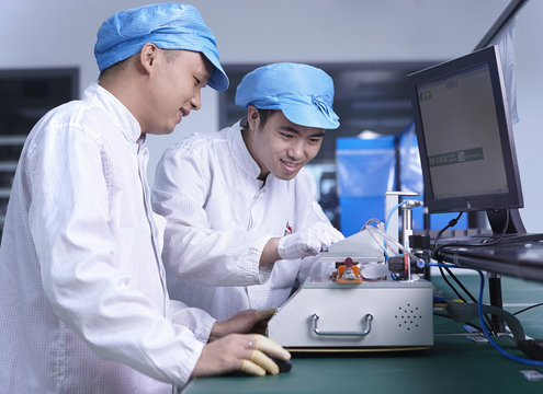 Workers using machinery in factory that specialises in creating functional circuits on flexible surfaces