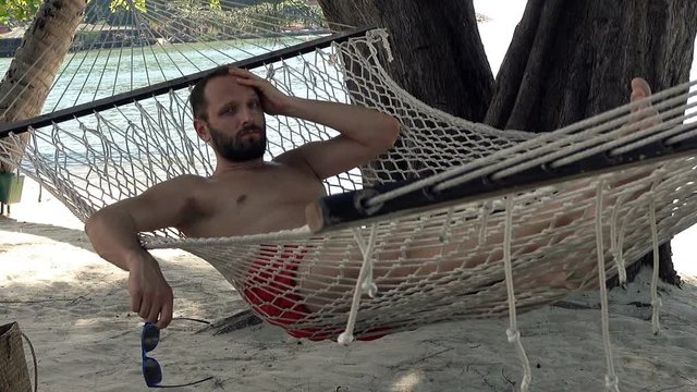 Sad, unhappy man lying on hammock on beach
