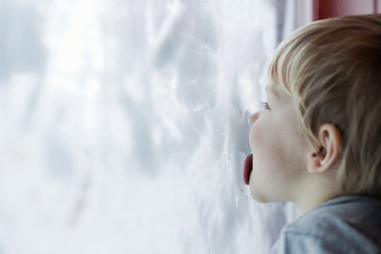 Boy licking inside of snow-covered window