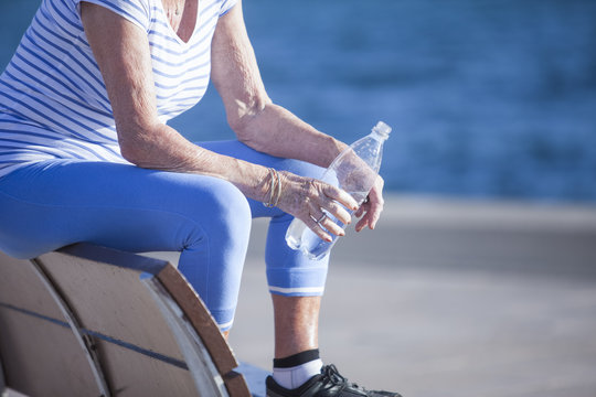 Senior woman sitting on bench by sea holding bottled water