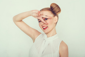 Beautiful girl with funny hairstyle. makes peace sign hands, smiling and showing tongue.