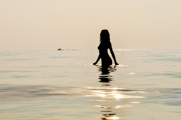 Girl silhouette at sunset in the water at seaside