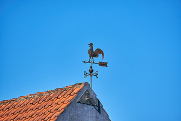 Fototapeta na wymiar Metal weathervane attached to the gabe of masonry house with red roof tiles