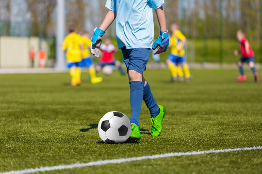 Young soccer player kicking ball in sports goalkeeper outfit