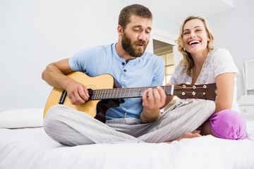 Man and woman playing guitar in bed