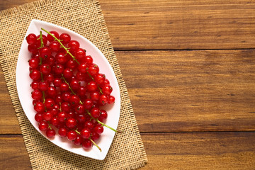 Rohe reife rote Johannisbeeren auf kleinem Teller, fotografiert auf dunklem Holz mit natürlichem Licht