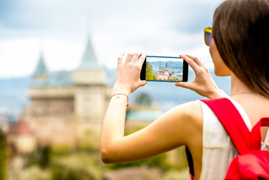 Young female traveler photographing with smart phone Bojnice castle in Slovakia