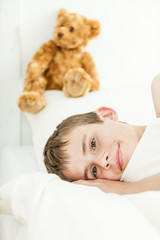 Smiling boy laying down near plush bear