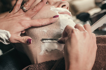 Female barber shaving a client's beard in a barber shop