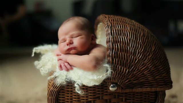 Adorable baby sleeping with his head resting on his hands in a vintage wicker buggy or cradle indoors the room