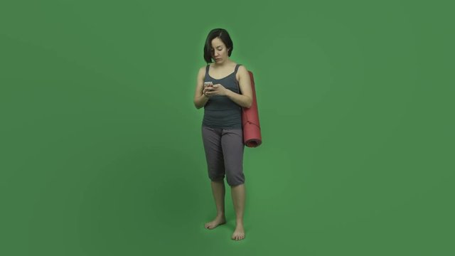 caucasian sporty girl with yoga mat isolated on green screen using cell phone