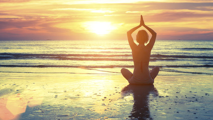 Fototapeta na wymiar Woman practicing yoga at seashore during sunset.