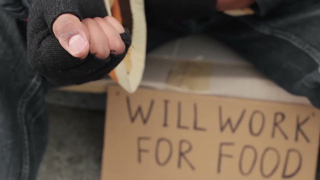 Poor man begging for change, holding coins in his hands, will work for food sign