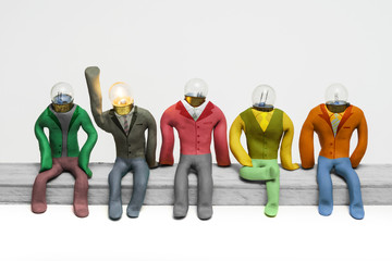 Clay executives figures with bulb head seated, having an idea