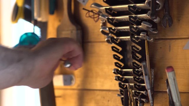 The male hand takes a fork spanner from a wall with the tool and then hangs up it back. 4K (UHD)