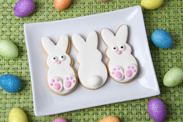Three Home made designer Easter Bunny Cookies on rectangular plate with green placemat, two baby...