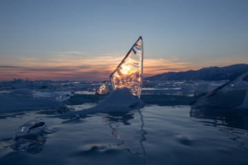 The setting sun is reflected in the transparent ice floe on Lake