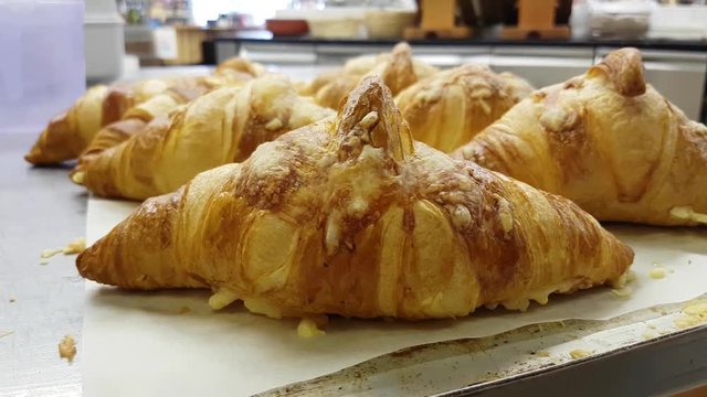 Lots of cheese topped croissants, at a bakery table