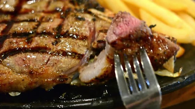 People eating juicy premium American prime rib steak with fork on a metal plate in HD. The focus is shallow depth of field. 