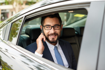 Cheerful successful man in car talking on phone