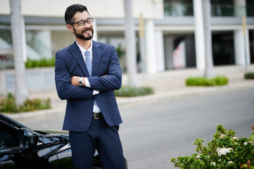 Happy entrepreneur standing at car with his arms folded