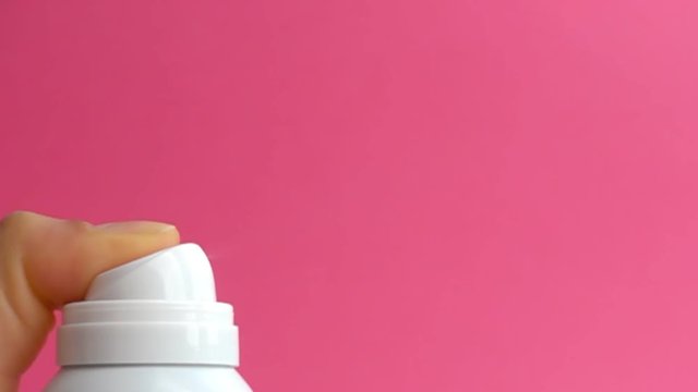 woman spraying aerosol deodorant in slow motion over pink background