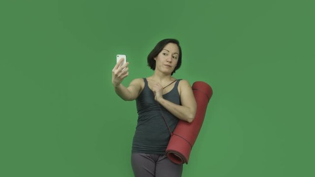 caucasian sporty girl with yoga mat isolated on green screen taking selfie