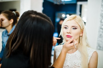 Young beautiful blonde bride applying wedding make up by makeup artist