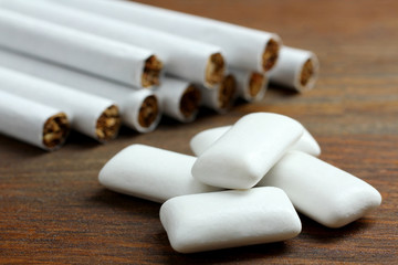 white chewing gum in the form of cushions on brown wooden background with a bunch of cigarettes