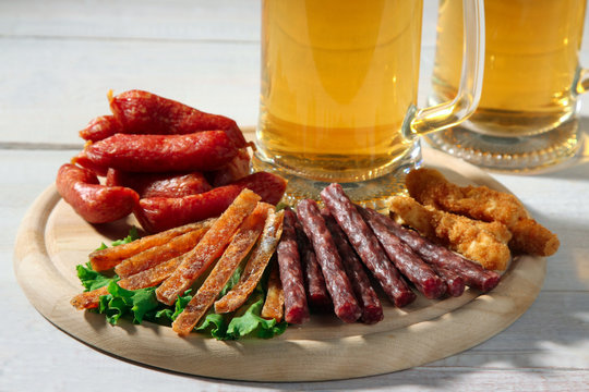light beer in glass with a variety of sausages in a wooden cutting Board on wooden white background