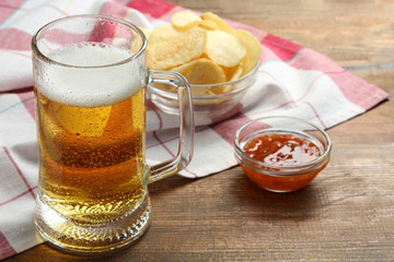 light beer in a glass with a bowl of chips and ketchup on a napkin on wooden brown background