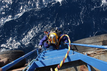 Obraz premium Photo of a diver in suit and helmet, which descends from the ship down to the water