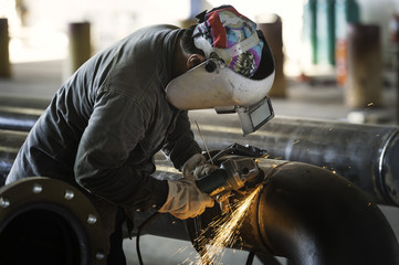 Worker using industrial grinder during grinding piping construct