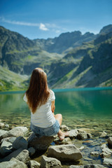young girl sitting on stone near mountain lake