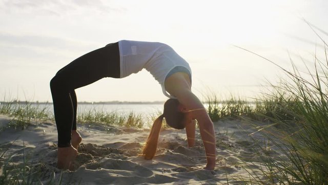 4K Young flexible woman in a wheel yoga pose on a beach, in slow motion