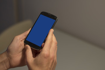 Hands holding mobile phone with blue screen.