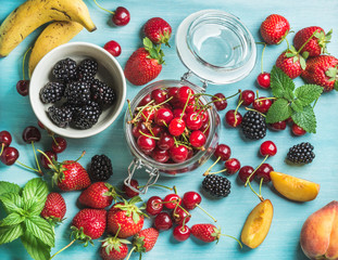 Healthy summer fruit variety. Sweet cherries, strawberries, blackberries, peaches, bananas and mint leaves on blue backdrop