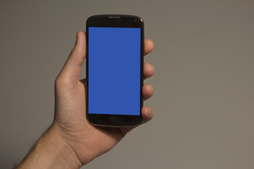  Hand holding smartphone with blue screen on grey background and