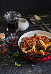 Italian pasta with eggplant and tomato sauce and a glass of red wine. On a dark wooden background. Healthy vegetarian food