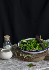 Fresh garden herbs in an enamel bowl on a wooden board on a dark background
