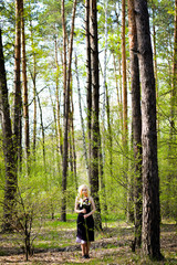 Beautiful smiling magic girl in the wood. Fashionable young short haired blond woman posing in the forest park wearing fancy empire style dress holding flowers. Concept of fantasy and magic.