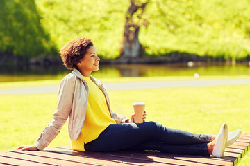 happy african woman drinks coffee at summer park 