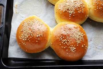 Tasty buns with sesame on oven-tray, on wooden background