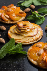 Tart with apricot and apple. Traditional french pie with fruits on dark marble background. Decorated almonds and mint leafs. Delicious dessert with copy space closeup.