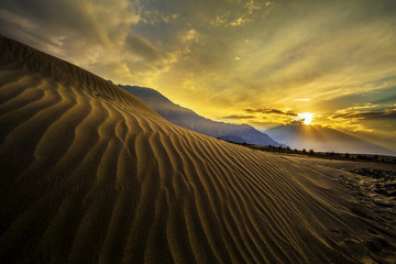Sun rise at sand dunes against the background of distant colorful mountain range and sunrise sky, Ladakh, Himalaya, Jammu & Kashmir, Northern India - obrazy, fototapety, plakaty