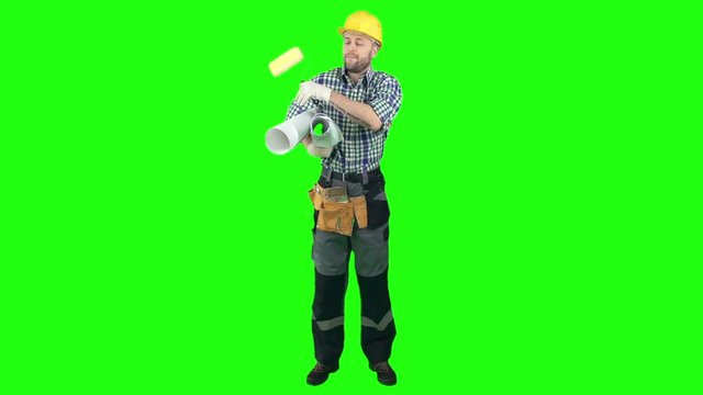 Workman in hardhat and uniform standing on green screen background, holding blueprint and roller and smiling