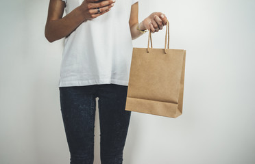 Young hipster girl holding blank craft package, mock-up of brown paper shopping bag with handles in...