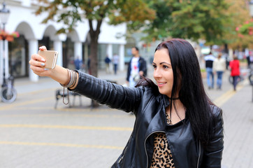 black hair woman in leather coat taking selfie photo on   street