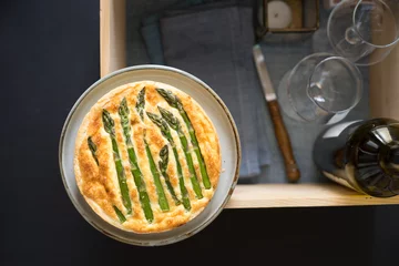 Möbelaufkleber Asparagus tart with egg and cheese filling on wooden box with glasses and wine bottle prepared for picnic. Selective focus on the tart surface. © inats